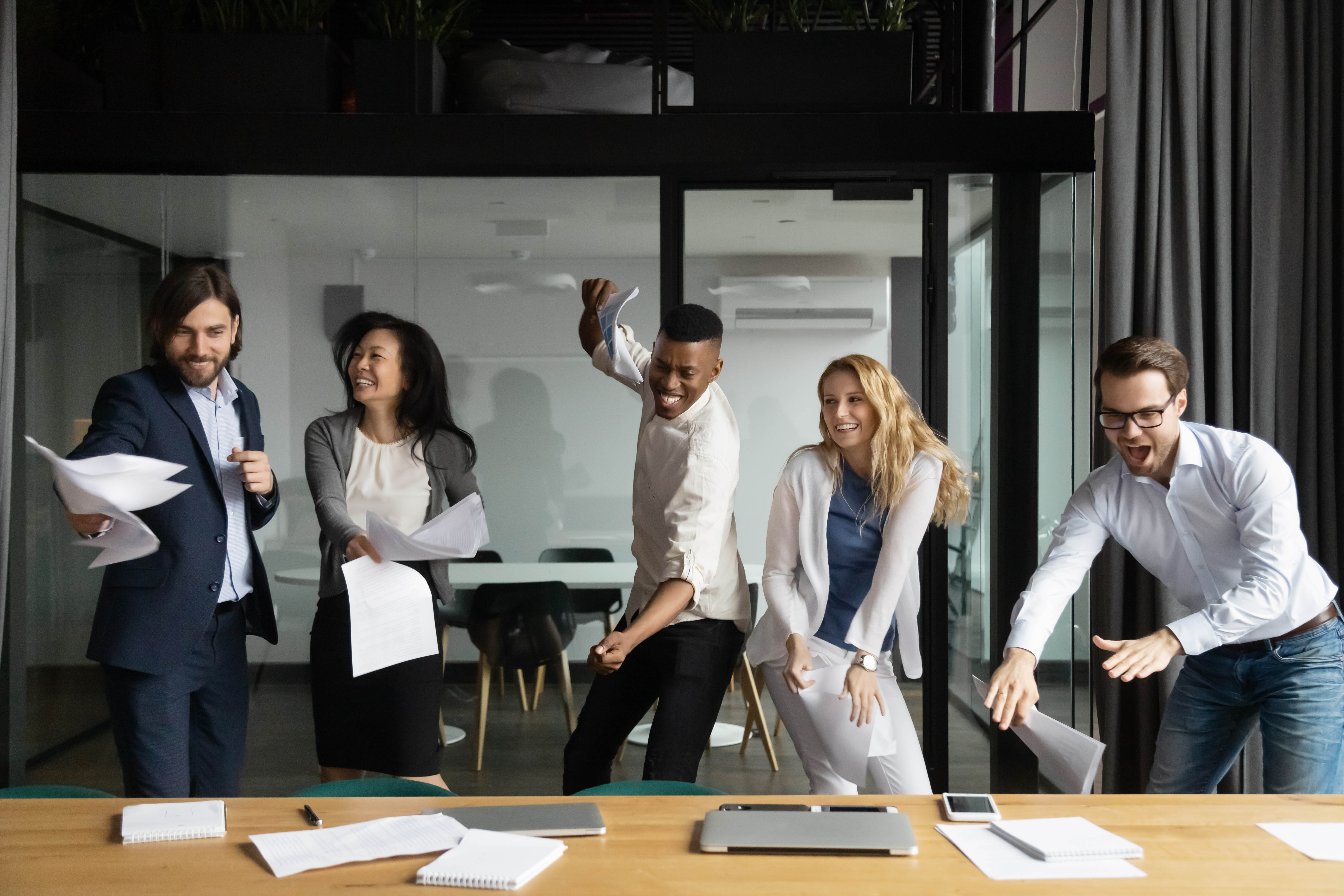 Male and female colleagues celebrating, laughing, and dancing in the office boardroom